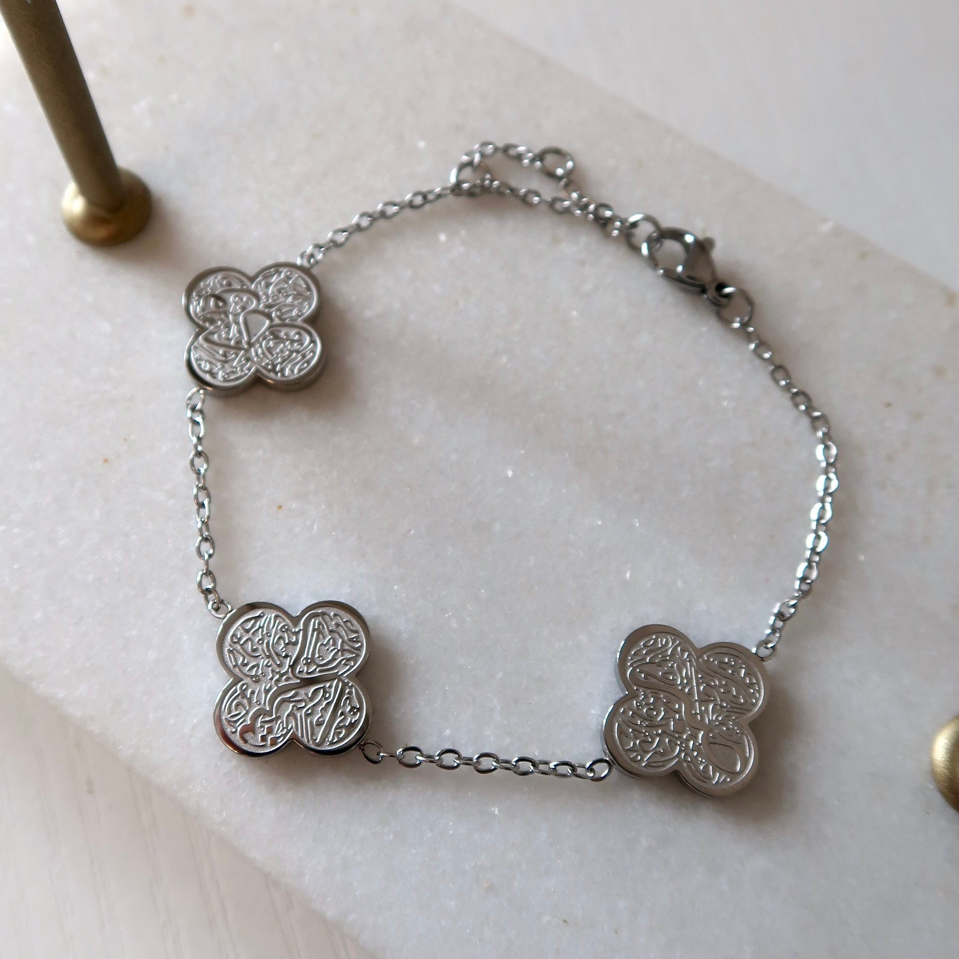 Silver bracelet with clover-shaped charms on a marble surface highlighting Sabr, Shukr and Tawakkul on each clover in arabic calligraphy